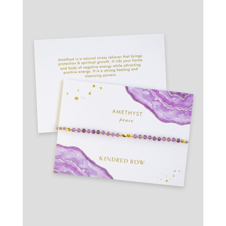 The Amethyst Healing Gemstone Stacking Bracelet by Kindred Row is a delicate piece featuring natural amethyst beads, elegantly presented on a card adorned with purple watercolor designs. This handmade bracelet includes an adjustable cord for added comfort. The accompanying card highlights the stress-relieving and healing properties of amethyst, along with the words "peace" and "Kindred Row.