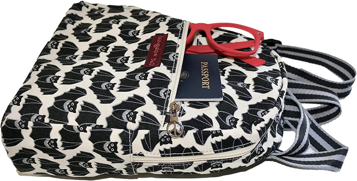 A partially opened Bungalow 360 "Backpack Bat," a cotton canvas backpack with a white and black bat pattern, reveals a navy blue passport and red-framed eyeglasses in its front zipper pocket. Known for its unique designs, the backpack also features black and white striped straps.