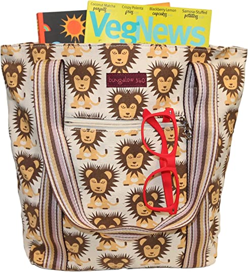The Bungalow 360 Striped Tote - Lion is a roomy cotton canvas bag featuring a lion print, striped handles, and a front zipper pocket—ideal for carrying two magazines and red glasses hanging from the pocket.