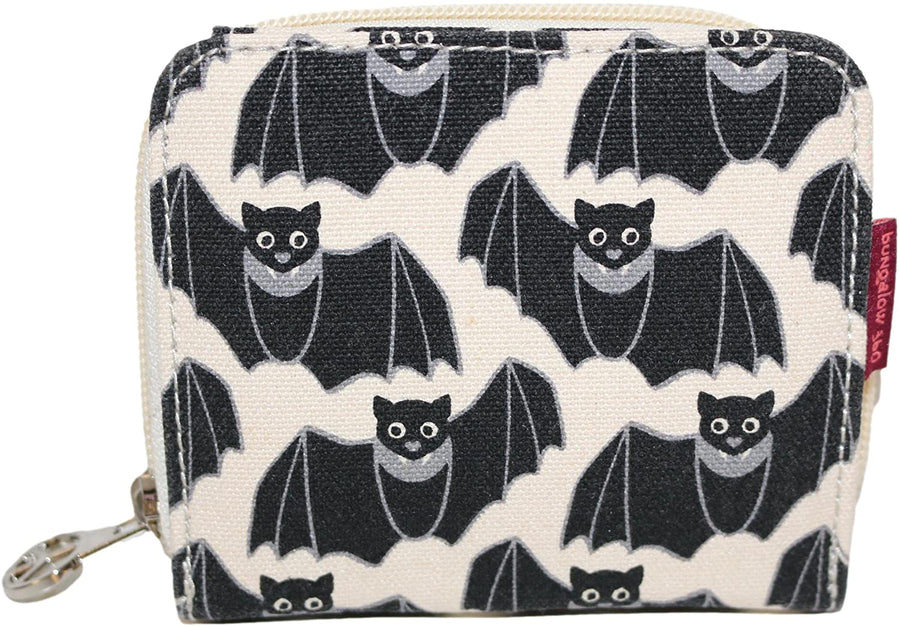 The Bungalow 360 Bill Fold Wallet Bat is a small zippered wallet crafted from cotton canvas, showcasing a distinctive black bat pattern on a cream background. The bats are depicted with wings spread open, smiling faces, and white eye details. It features a metallic zipper pull and a reddish-brown tag attached to the side. This vegan accessory blends style with conscious living.