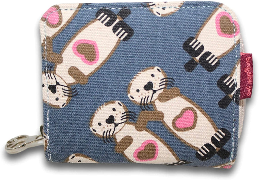 The Bill Fold Wallet Sea Otter by Bungalow 360 showcases a small blue coin purse adorned with a delightful pattern of cartoon otters holding pink heart shapes on their chests. This charming accessory, crafted from vegan cotton canvas, features a metal zipper and a distinctive red fabric tag on the side, highlighting its unique design.