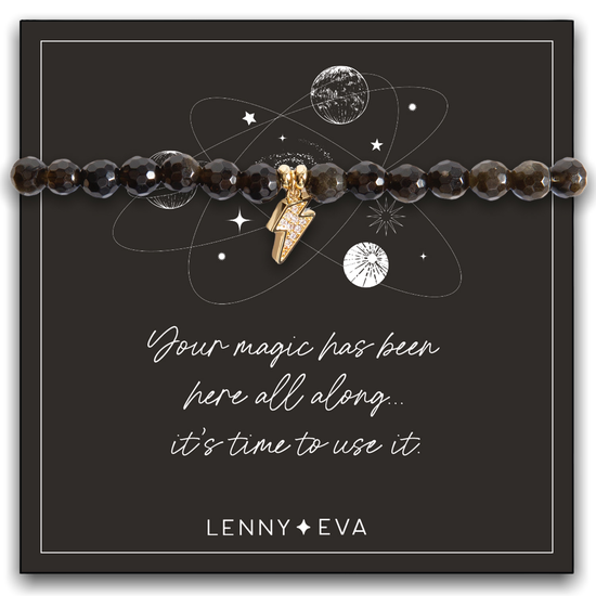 The Celestial Bracelet-Bolt, adorned with luxurious golden obsidian beads and a lightning bolt charm, is presented on a card featuring a cosmic design. The text reads, "Your magic has been here all along... it's time to use it," embodying the spirit of the Celestial Collection. The brand name "Lenny & Eva" appears elegantly at the bottom.