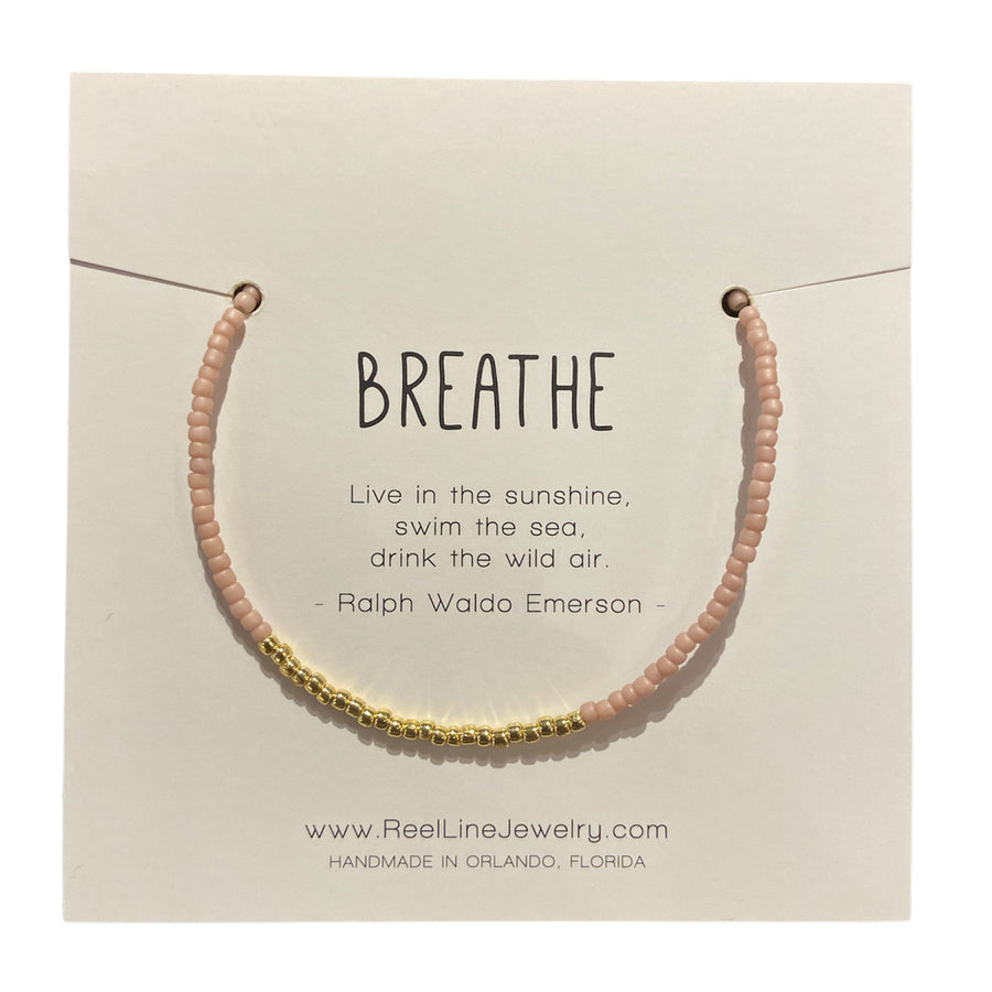 The "Breathe - Pink Gold" bracelet from Reel Line Jewelry is beautifully presented on a card. This handcrafted piece from Orlando, Florida, showcases an elegant combination of pink and gold glass beads, complete with adjustable links for the perfect fit. It features a quote by Ralph Waldo Emerson.