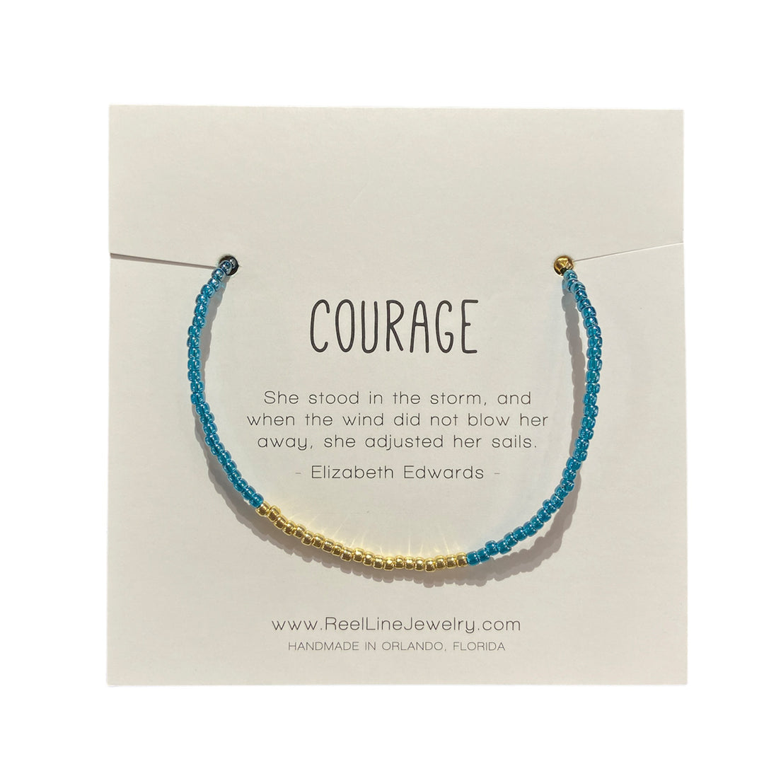 A carefully crafted Glass Beaded Bracelet, featuring teal and gold beads, is elegantly displayed against a card. The card bears the inspiring quote: "COURAGE. She stood in the storm, and when the wind did not blow her away, she adjusted her sails. - Elizabeth Edwards." This beautiful piece is made by Reel Line Jewelry in Orlando, Florida.