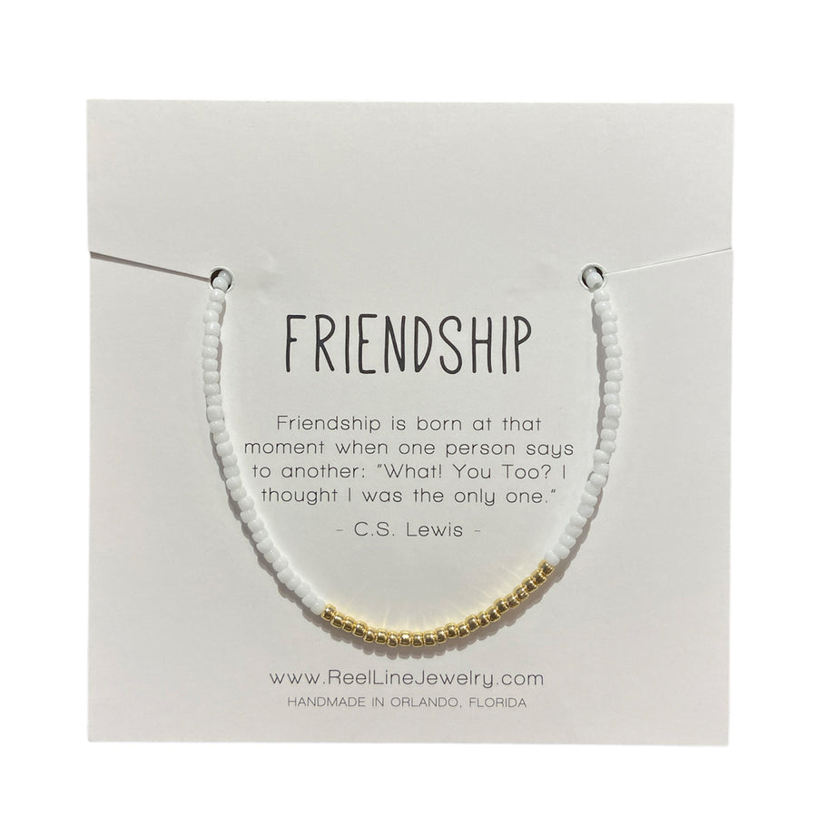 The "Friendship - White Gloss Gold" glass beaded bracelet by Reel Line Jewelry is elegantly displayed on a card featuring a quote about friendship by C.S. Lewis. This handcrafted jewelry, made in Orlando, Florida, comes with adjustable links.