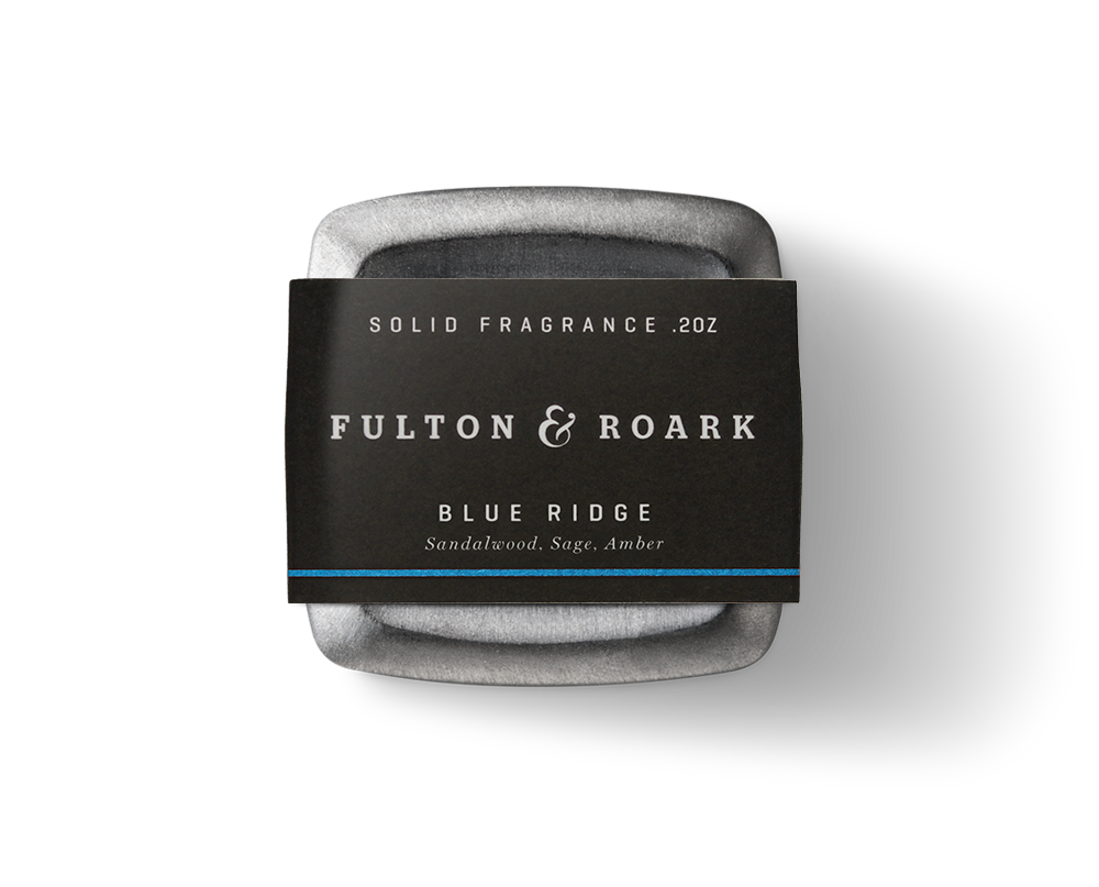 A .2oz tin of Fulton & Roark solid fragrance in the captivating "Blue Ridge" scent, featuring sandalwood, sage, and amber. The packaging is sleek black with crisp white text.