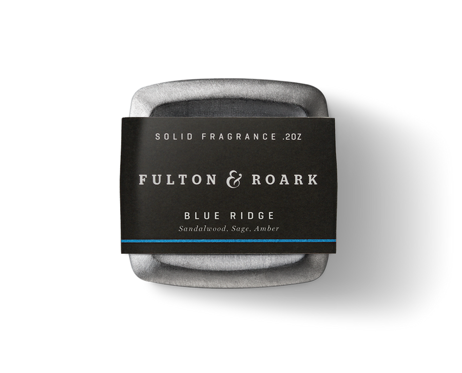 A .2oz tin of Fulton & Roark solid fragrance in the captivating "Blue Ridge" scent, featuring sandalwood, sage, and amber. The packaging is sleek black with crisp white text.