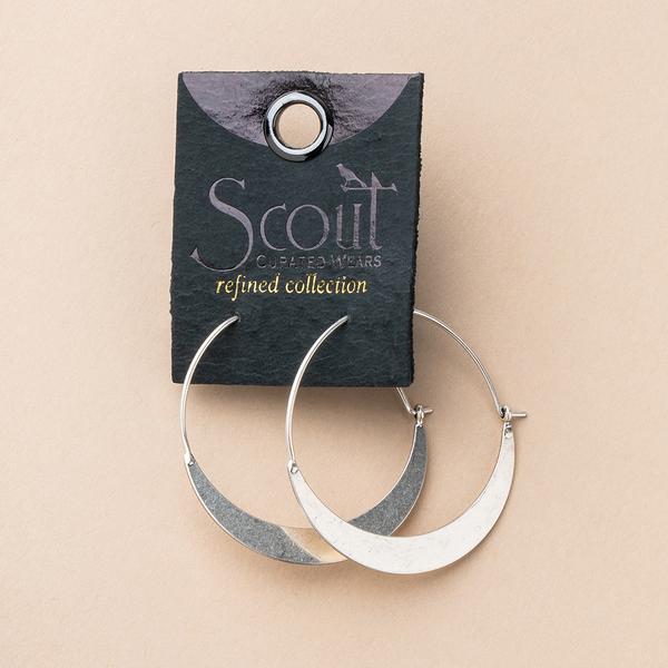 A pair of gold hoop earrings attached to a black tag labeled "Scout Jewelry, refined collection." The tag has a small hole at the top for hanging. Hypoallergenic and nickel-free, the Crescent Hoop Gold earrings have a sleek, modern design with a partially flat lower section.