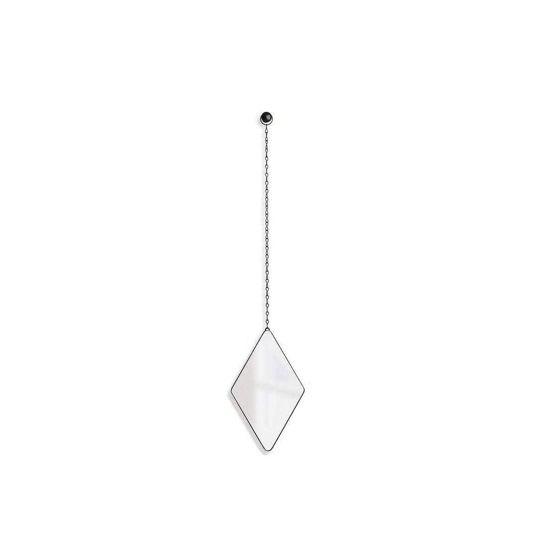 An inverted diamond-shaped Diamond Mirror Black by Umbra hangs from the wall by a metallic chain attached to a circular hook at the top. The mirror's thin black frame is suspended against a plain white background, introducing a button-like quality to the sleek hardware decor.