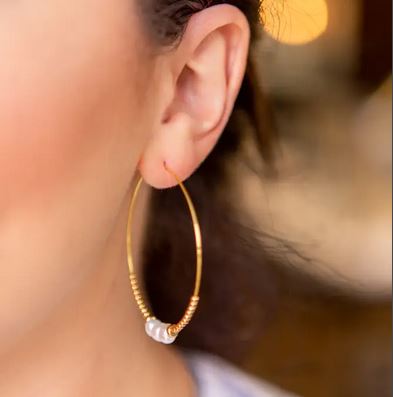 Close-up of a person's ear wearing the Amazonite Lily Earrings from Lenny & Eva, featuring gold hoops adorned with small pearls lining the bottom. This piece of handcrafted jewelry stands out against the softly blurred background.