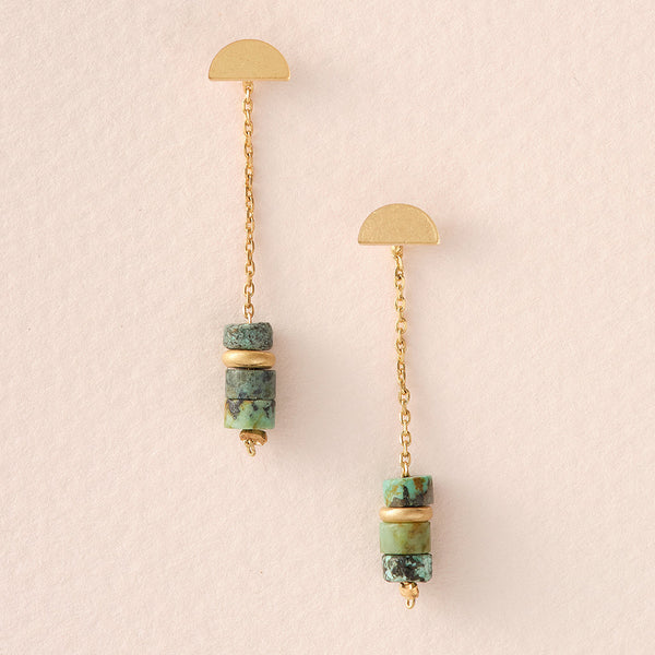 Introducing the Meteor Thread African Turquoise Gold earrings by Scout Jewelry: an elegant pair of 14K gold drop earrings featuring semicircular studs and hanging chains adorned with stacked beads in green and gold tones. These hypoallergenic earrings are beautifully presented against a neutral beige background.