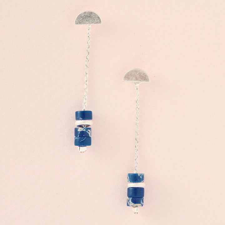 The Meteor Thread Lapis Silver earrings by Scout Jewelry feature sterling silver half-circle tops with chains adorned with blue and white bead clusters. They're nickel- and cadmium-free, hypoallergenic, and designed for sensitive ears, offering subtle elegance against a pale background.