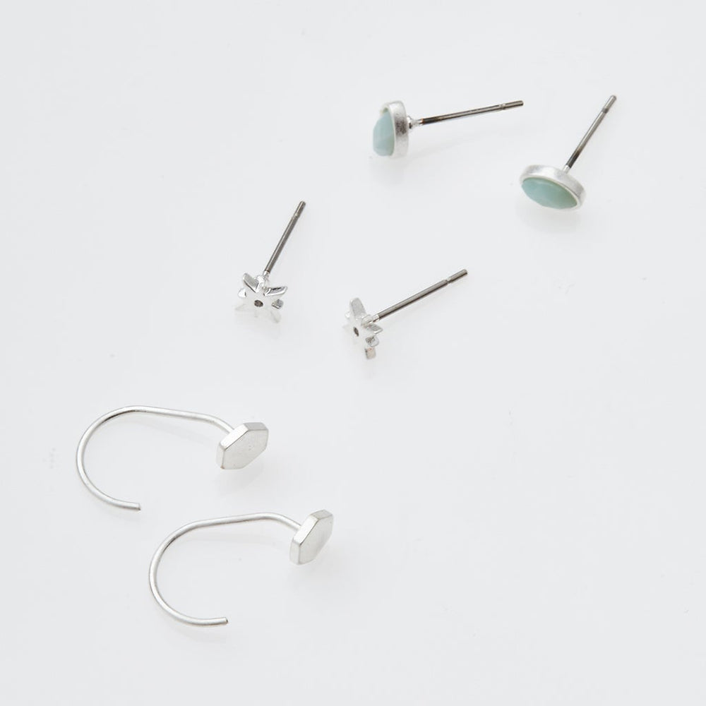 The Gabby Stud Trio Silver by Scout Jewelry, featuring hypoallergenic turquoise stones in a pair of silver studs, is elegantly displayed alongside a minimalist pair of silver hoop earrings on a white surface.