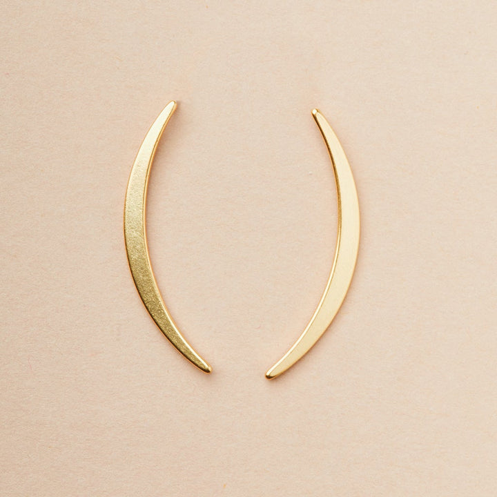 The 18k gold vermeil Gibbous Slice Stud Gold earrings from Scout Jewelry's Refined Earring Collection elegantly rest on a simple beige background, arranged symmetrically to face one another.