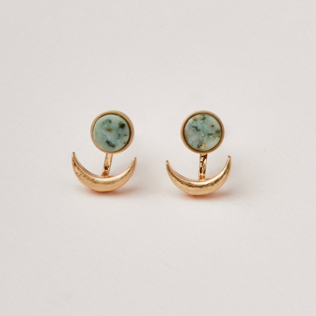 The Moon Phase African Turq/Gold earrings by Scout Jewelry showcase circular gemstones with a delicate light blue-green pattern as studs, each paired with an adjustable brass crescent moon design hanging below. Displayed against a plain white background, these hypoallergenic earrings are both stylish and comfortable for sensitive ears.