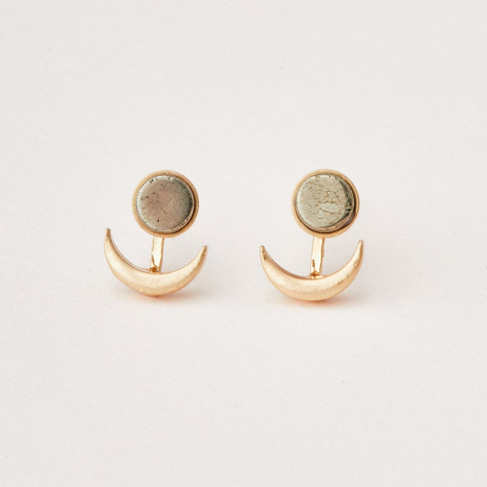 A pair of Moon Phase Pyrite/Gold earrings from Scout Jewelry lies on a white background. Each earring features a crescent shape beneath a textured round disk, connected by a slim gold bar. The organic look of the textured disks makes these hypoallergenic accessories ideal for any occasion.