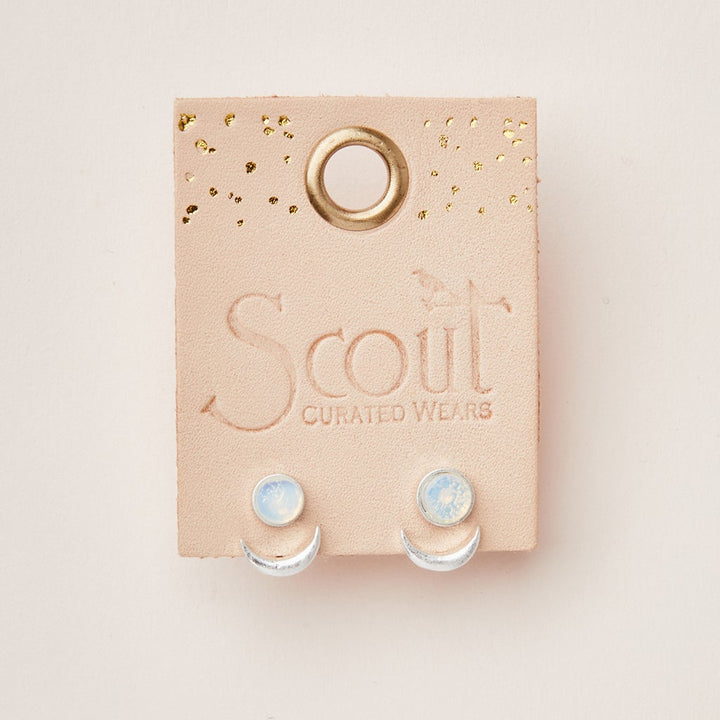 A pair of semi-precious Moon Phase Amazonite/Gold earrings is displayed on a beige leather card embossed with "Scout Jewelry." The earrings feature a small round amazonite at the top with an adjustable brass crescent ear jacket underneath. The card is adorned with gold speckles and has a loop hole at the top.
