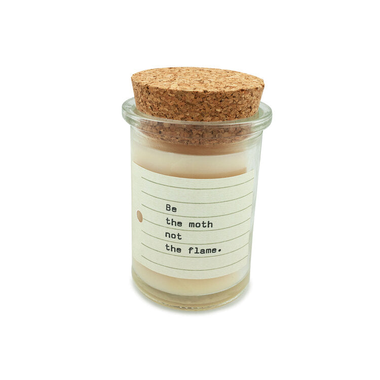 The Skeem Field Jar Tobacco Musk is a pale cream soy wax candle in a glass jar with a cork lid, offering a 35-hour burn time. It features warm spices and bears the label "Be the moth not the flame" with elegant horizontal lines and a small dot.