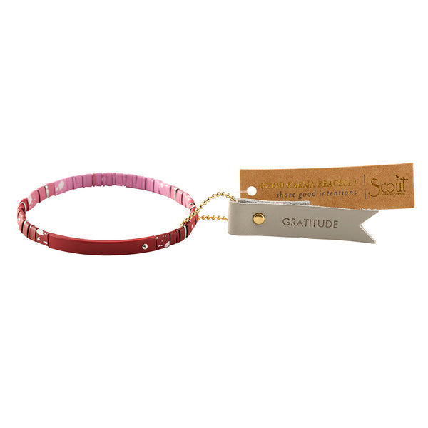 Introducing the Good Karma Ombre Gratitude Mulberry Silver bracelet from Scout Jewelry, a stylish accessory featuring empowering messages. This pink and red beaded bracelet includes matte ombre tile beads and tags attached by a small gold chain. The tags read "GRATITUDE" and "Scout," with an additional note "Scout CURATED WEARS" on the left.