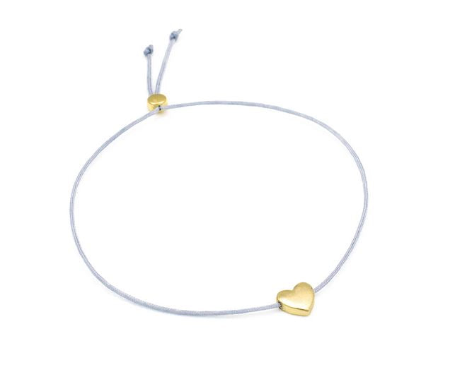 The Love Birthday bracelet from LuckyFeather is a delicate silver piece featuring an adjustable knot, perfect for a birthday gift, and adorned with a small gold heart charm.