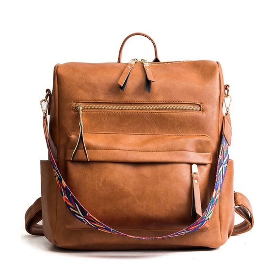 Introducing the Hailey Backpack - Brown by zzzLivFoxy: A chic brown vegan leather backpack with versatile pockets, highlighted by gold zippers and a vibrant, adjustable woven shoulder strap. This design seamlessly blends practicality with lively details.