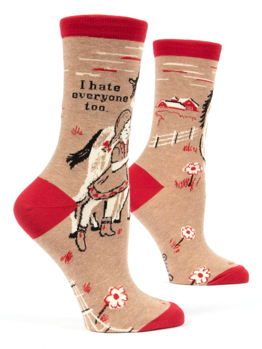 Beige and red women’s socks, available in sizes 5-10, crafted from soft combed cotton. These "I hate everyone Socks" by Blue Q feature a whimsical illustration of a girl riding a white horse against a countryside scene with a barn and fence, alongside the text "I hate everyone too.