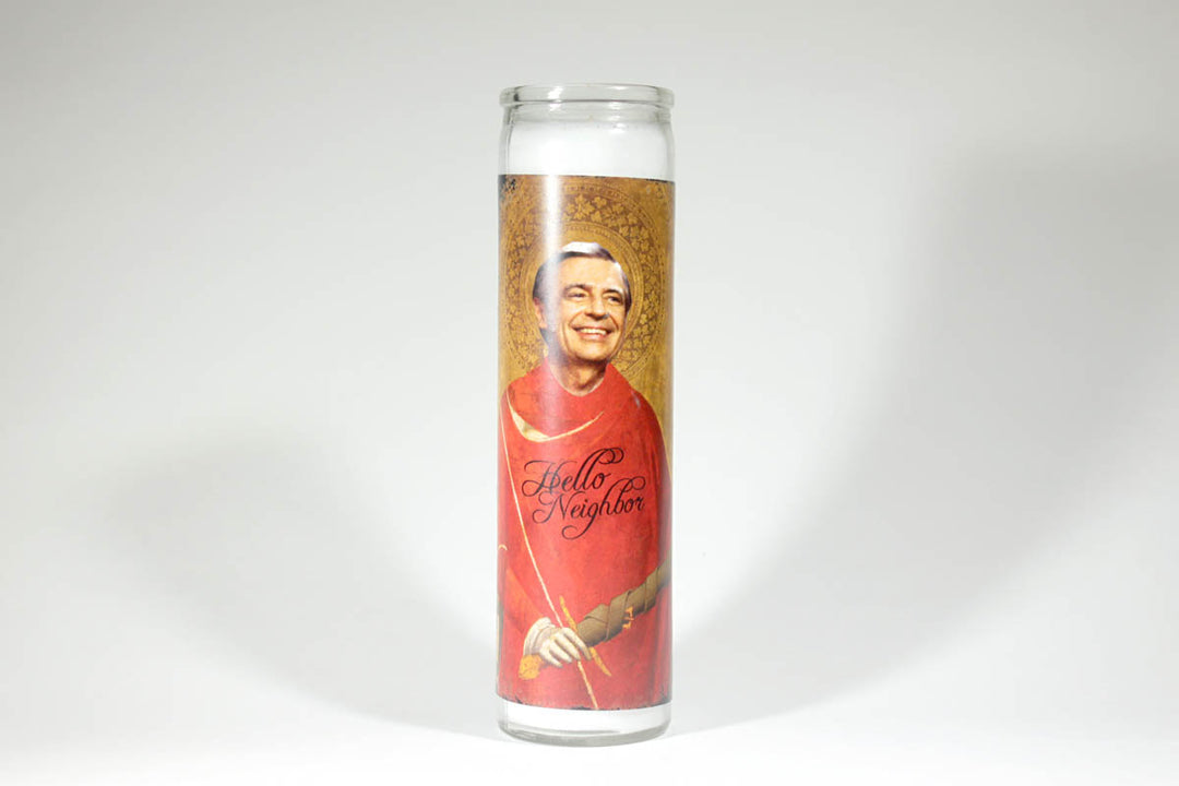 The BOBBYK BOUTIQUE "Mr. Rogers Candle" features a smiling man in a red robe and mitre, embodying Mr. Rogers' friendly neighbor spirit. "Hello Neighbor" is elegantly scripted on the robe against a plain white background.