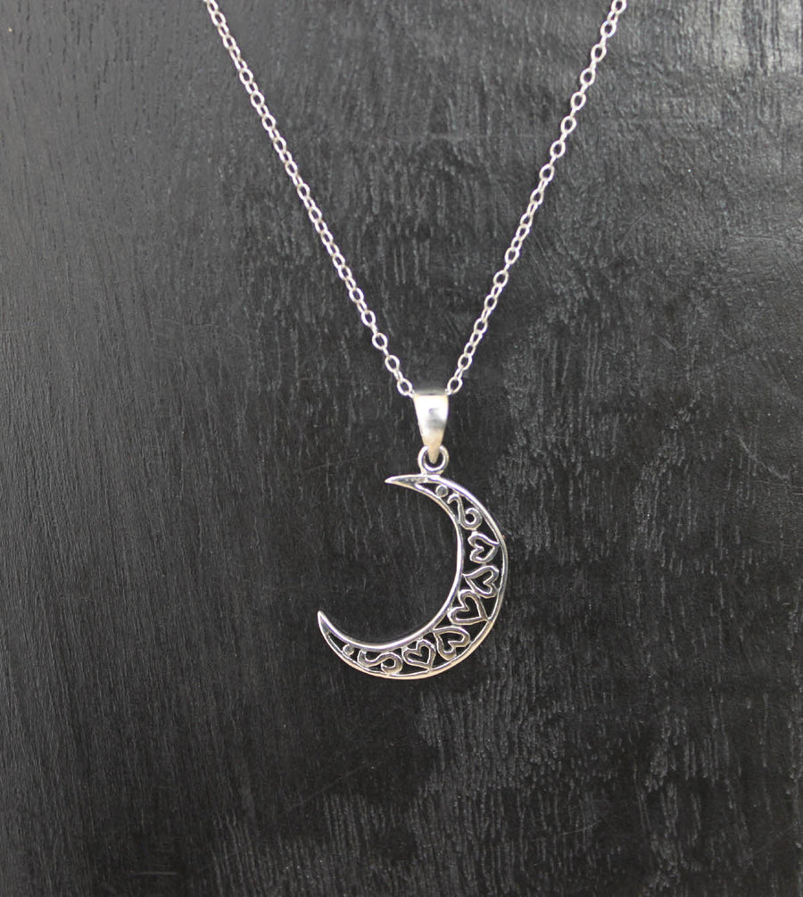 A delicate sterling silver necklace with a Heart Moon pendant by Welman is displayed against a dark background. The 925 Sterling Silver pendant features intricate filigree work, giving it an elegant and ornate appearance. The fine sterling silver chain is thin and complements the design of the pendant perfectly.