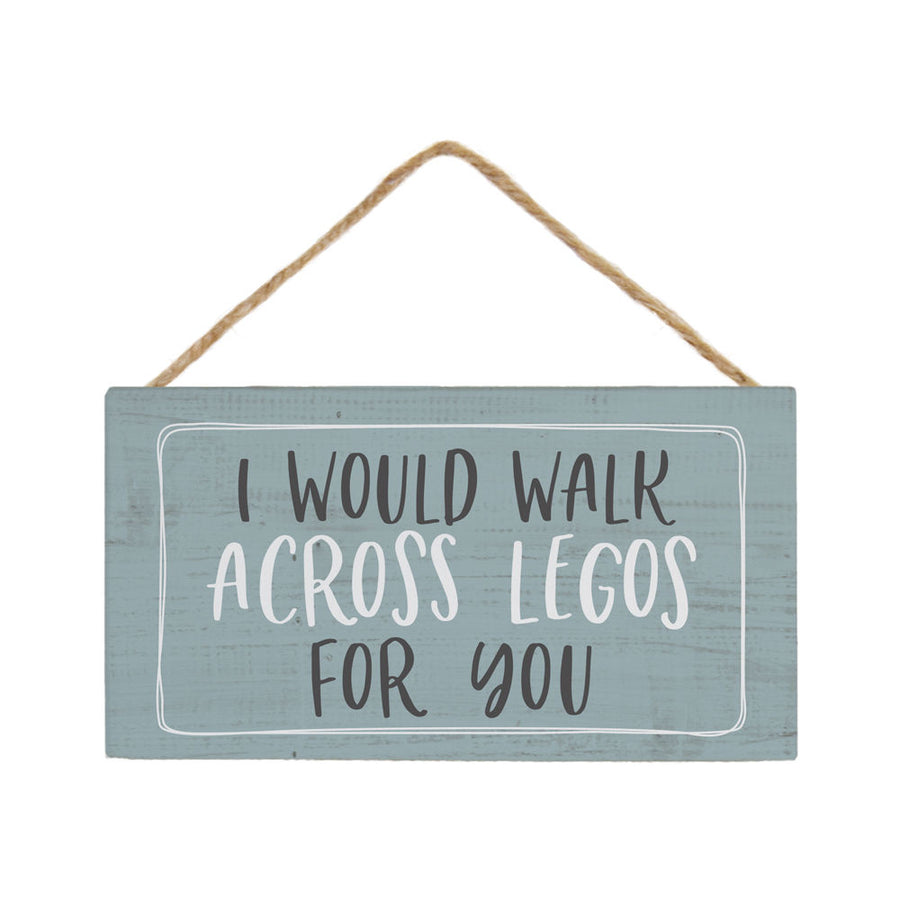 A handcrafted ornament by SincereSurroundings, the "I Would Walk" sign is a rectangular light blue wooden piece with a rustic finish, hung by a braided twine string. It features bold black and white text that reads: "I WOULD WALK ACROSS LEGOS FOR YOU.