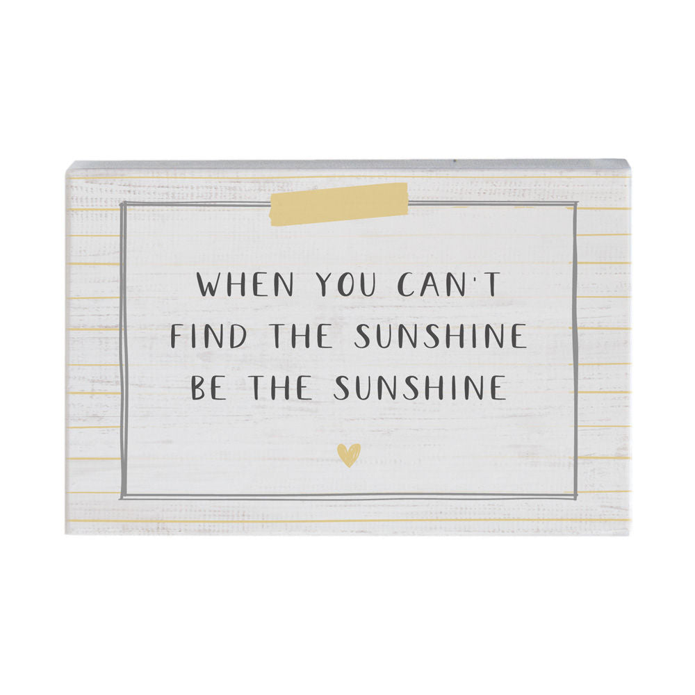 The "Be the Sunshine" handcrafted wooden plaque by SincereSurroundings features a white background with subtle horizontal stripes and displays the text, "When you can't find the sunshine be the sunshine" in a neat, printed font. A small yellow heart adorns the bottom of the plaque, while a piece of yellow tape at the top adds extra charm. It's easy to display in any Rock Rapids home.