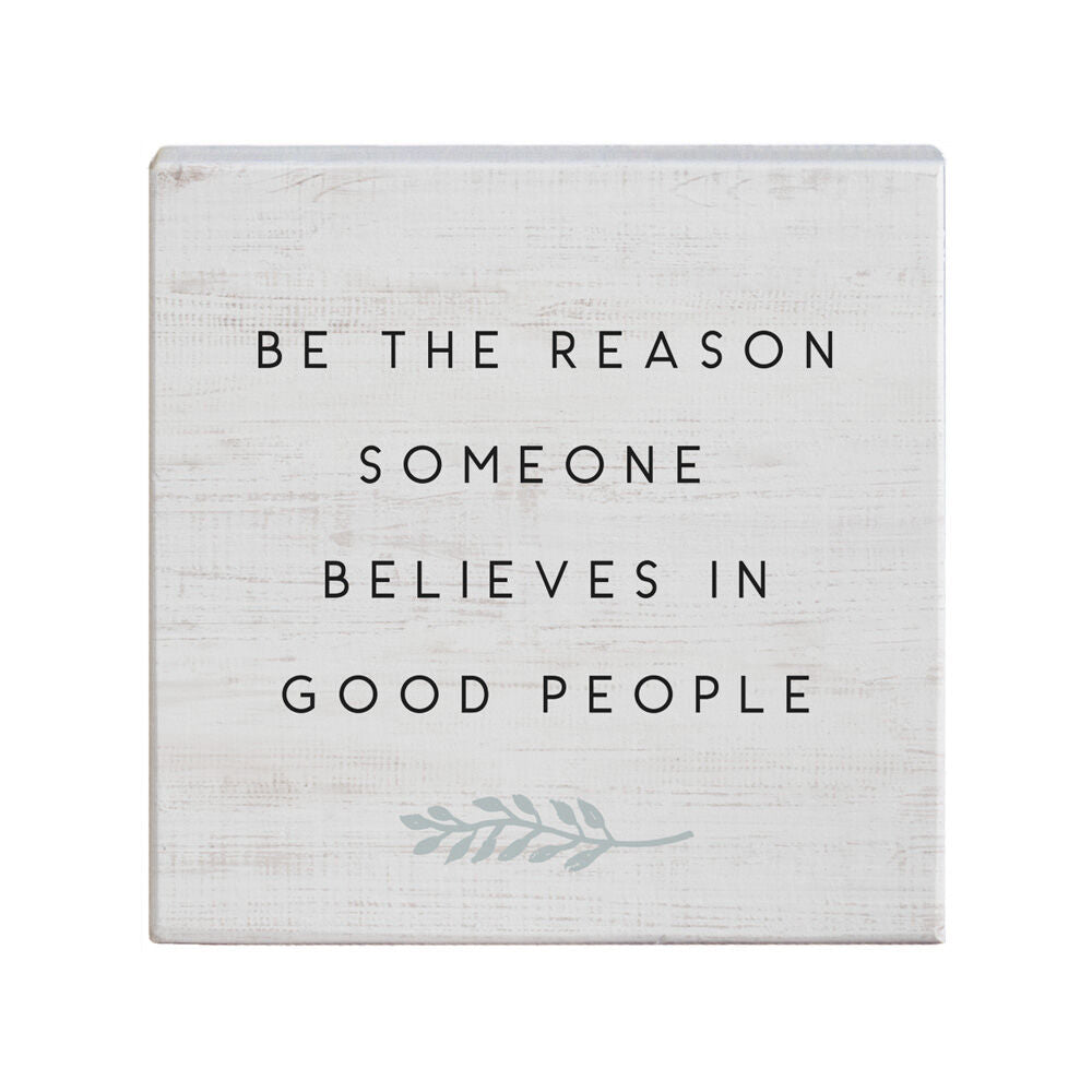 The Believes In Good sign from SincereSurroundings features a square design with a white, rustic, wood-like texture. It displays the phrase "Be the reason someone believes in good people" in black, uppercase letters. Perfect for a shelf display, it also includes a simple graphic of an olive branch in light gray, adding to its handcrafted charm.