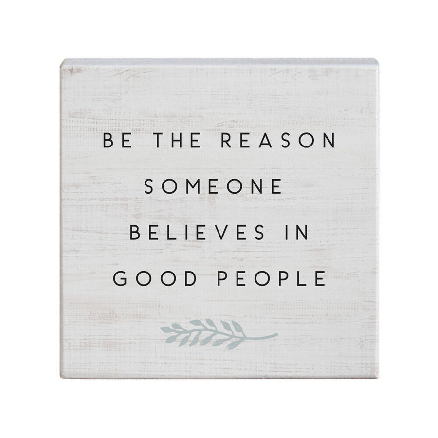 The Believes In Good sign from SincereSurroundings features a square design with a white, rustic, wood-like texture. It displays the phrase "Be the reason someone believes in good people" in black, uppercase letters. Perfect for a shelf display, it also includes a simple graphic of an olive branch in light gray, adding to its handcrafted charm.