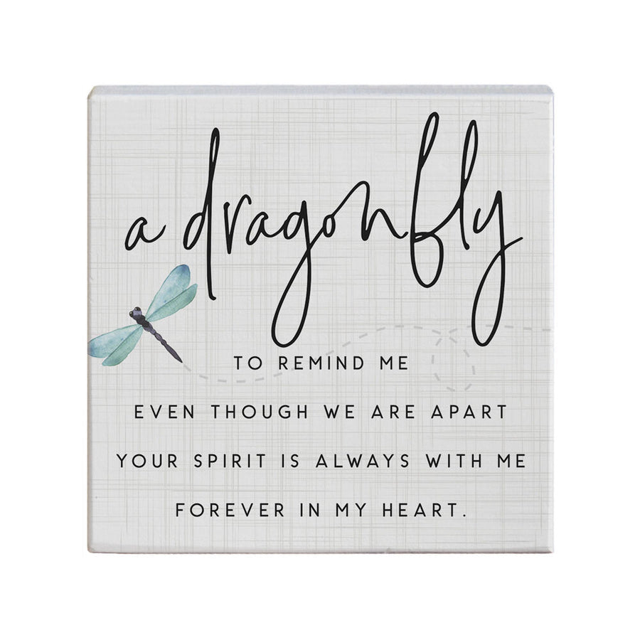 The "Dragonfly To Remind" plaque by SincereSurroundings is a small, handcrafted piece featuring an image of a dragonfly and a heartfelt message in cursive and printed text: "A dragonfly to remind me, even though we are apart, your spirit is always with me, forever in my heart." The background has a subtle grid pattern for easy display.