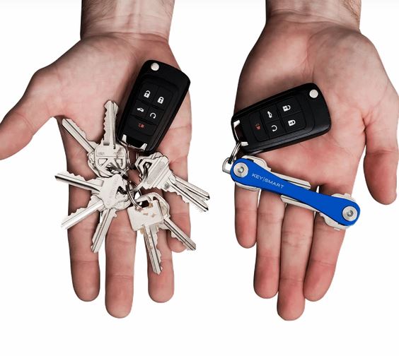 Two hands are shown. The left holds several keys on a keyring with a car key remote. The right hand holds the KeySmart Key Holder Blue, which eliminates key jingle and keeps everything organized with the car key remote attached.