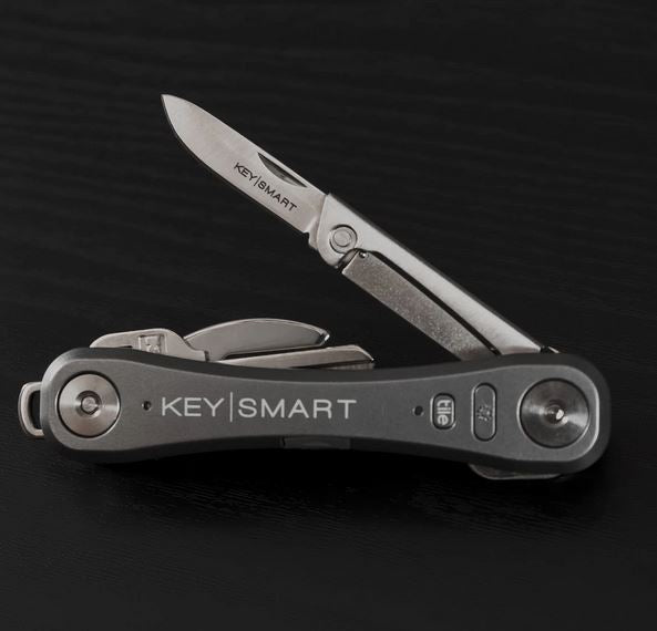 The KeySmart Mini Knife, a versatile multi-tool branded "KeySmart," features a partially open folding knife blade, a bottle opener, and additional folding tools. Ideal for any cutting task, this tool is showcased against a dark background.