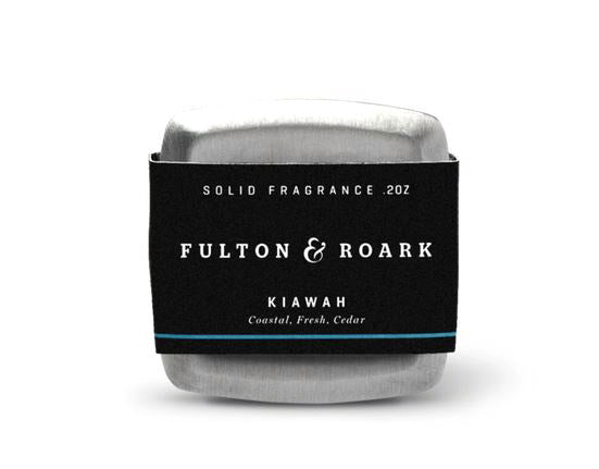 The Kiawah .2oz solid fragrance tin, crafted by Fulton & Roark, offers a unique blend of coastal freshness and Virginia Cedar undertones. It comes in a sleek silver container embellished with a black and blue label, perfectly capturing the essence of this distinct fragrance combination.