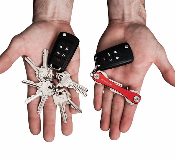 Two hands holding different sets of keys. The left hand holds a bundle of traditional metal keys with a car key fob, while the right hand holds the KeySmart Key Holder Red by KeySmart, making it comfortable to carry and keep your keys organized.