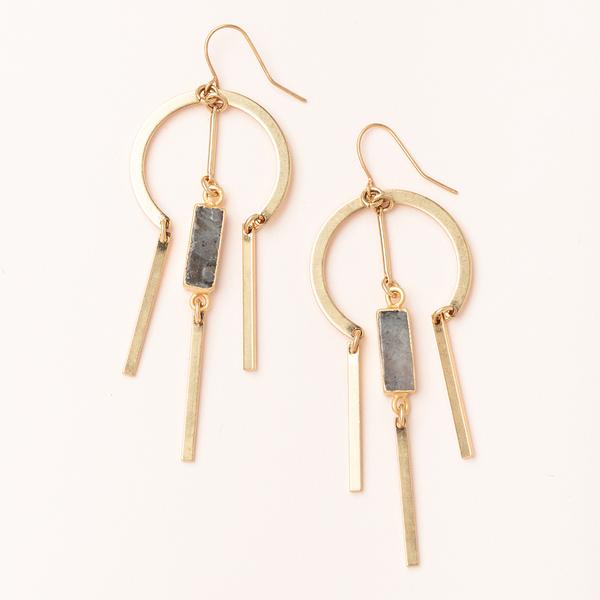 The Dreamcatcher Earring Labradorite Gold from Scout Jewelry is expertly crafted with 14k gold, showcasing geometric circular and rectangular elements. These exquisite earrings are embellished with hanging metal bars and stone-like rectangular pieces, offering a stunning accessory that is both nickel and cadmium free, set against a light beige background.