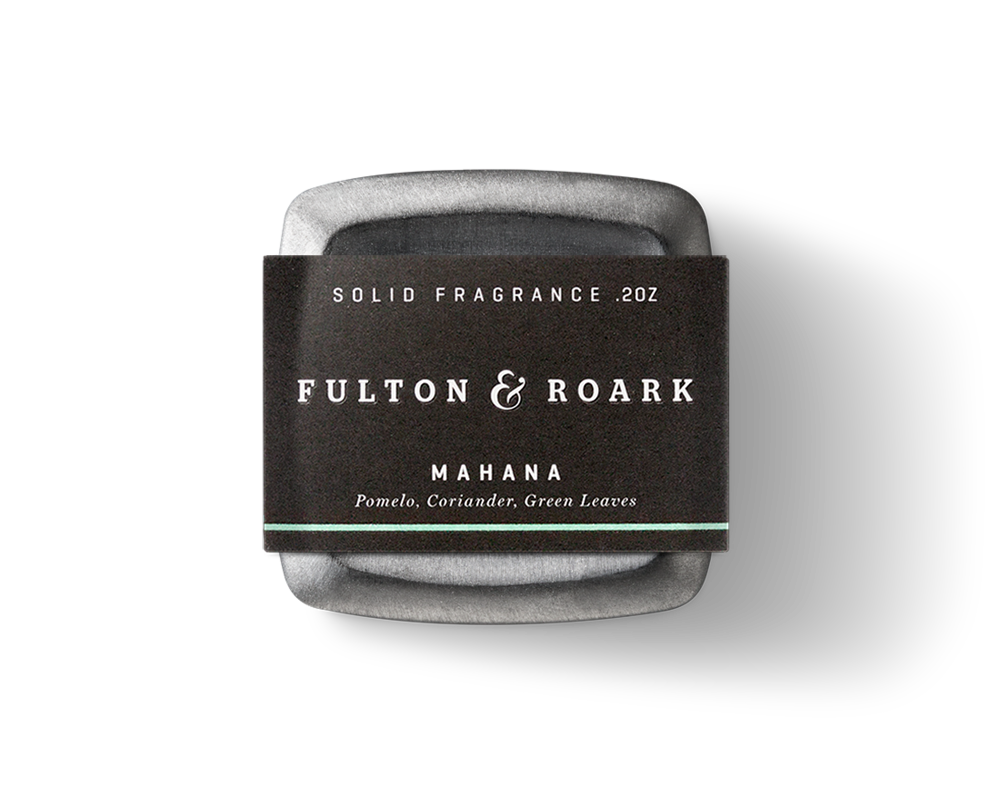 Fulton & Roark's Mahana solid fragrance, weighing 0.2 ounces, is housed in a square metal container with a black label. The fragrance captures the essence of Green Sand Beach with notes of pomelo, coriander, and green leaves, reminiscent of Papakolea's lush surroundings.