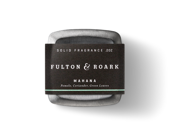Fulton & Roark's Mahana solid fragrance, weighing 0.2 ounces, is housed in a square metal container with a black label. The fragrance captures the essence of Green Sand Beach with notes of pomelo, coriander, and green leaves, reminiscent of Papakolea's lush surroundings.