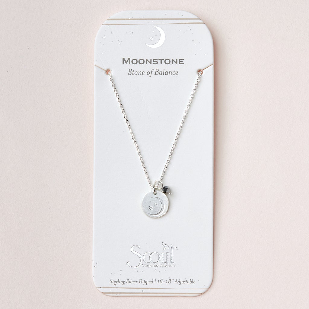 The Intention Neck Moonstone/Silver by Scout Jewelry is a silver necklace featuring a stunning circular moonstone pendant, elegantly presented on a white card with the inscription "Moonstone: Stone of Balance." It includes an adjustable brass chain marked with the brand's name "Scout," embellished with decorative moon illustrations, and boasts the Sterling Silver Dipped 16-18 inches feature.