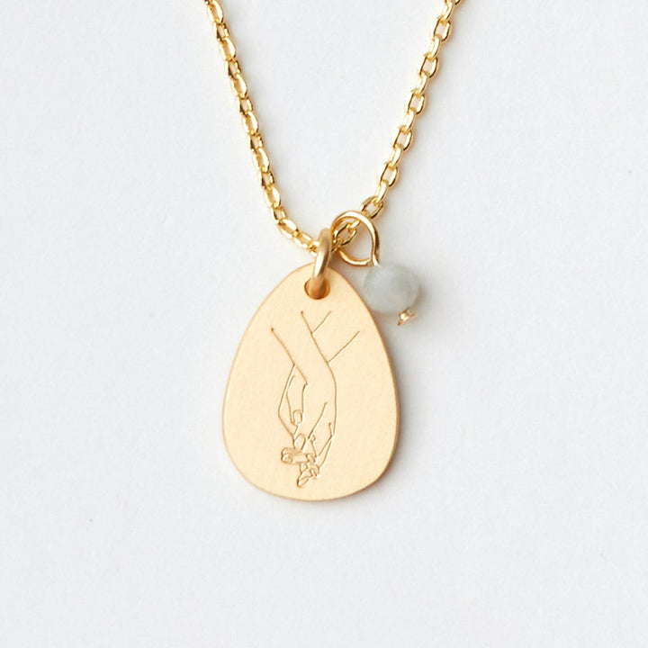 The Scout Jewelry Intention Neck features a teardrop pendant with an engraved design of two hands, paired with a small translucent Amazonite bead. The gold-plated chain is lightweight and adjustable for the perfect fit.