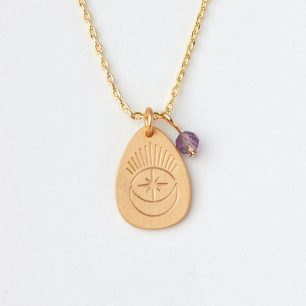 Introducing the "Intention Neck Amethyst/Gold" by Scout Jewelry: a gold necklace featuring an engraved teardrop-shaped pendant with a crescent moon and starburst design. The pendant includes a small purple semi-precious amethyst stone, all elegantly suspended from a fine, adjustable brass chain. Displayed beautifully against a plain white background.