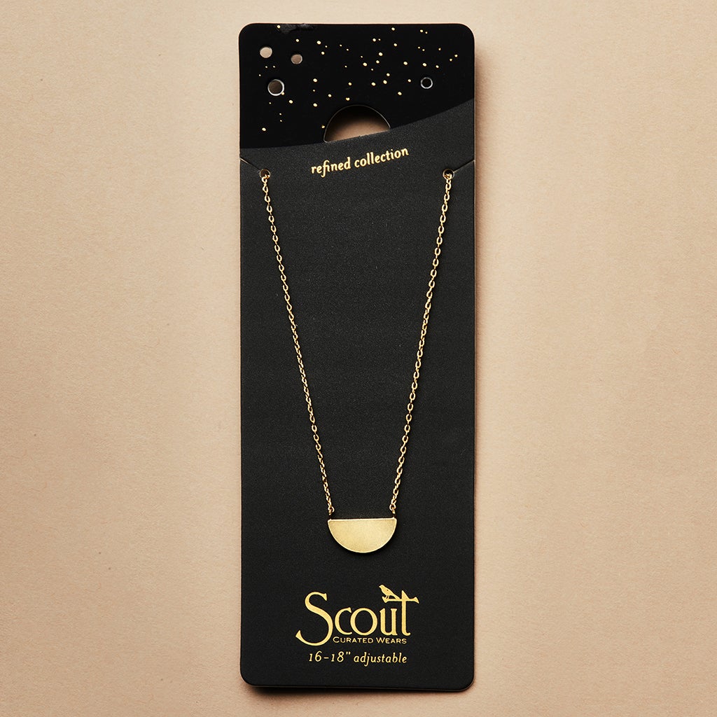 The "Refined Neck Half Moon/Gold" necklace by Scout Jewelry, featuring a gold half-circle pendant crafted from 18k gold vermeil, is elegantly presented on black packaging labeled "Scout Curated Wears, Refined Collection." The adjustable chain can be set from 16 to 18 inches in length, with a starry design adorning the top of the packaging.