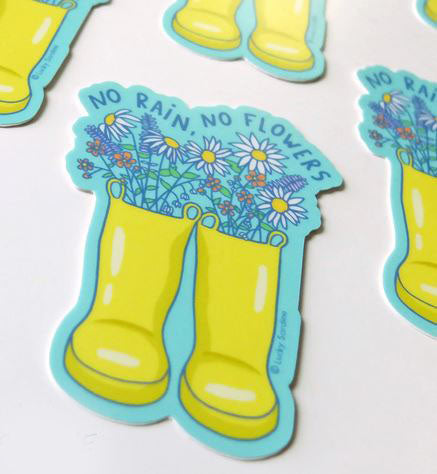 Introducing the "No Rain No Flowers Sticker" by Lucky Sardine. This durable vinyl sticker showcases a pair of yellow rain boots filled with vibrant flowers, set against a light blue border. Above the boots, in all caps, is the motivational text "NO RAIN NO FLOWERS". The weatherproof design also features additional identical stickers partially visible around it.