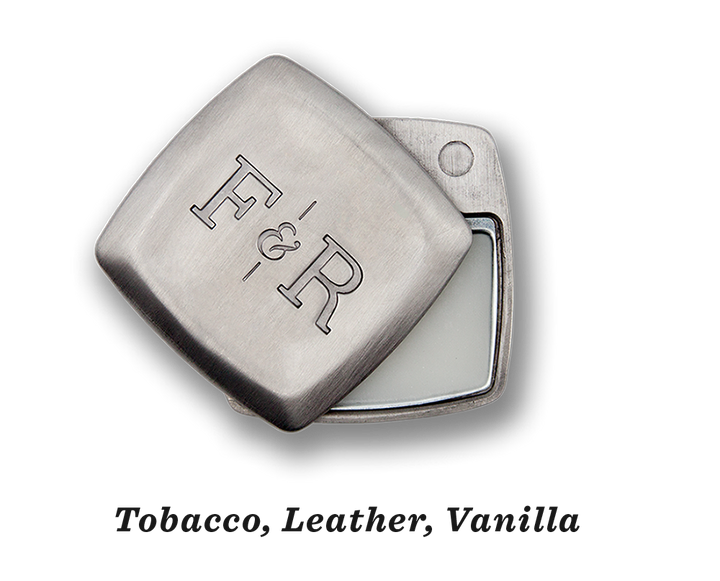 The image displays a compact, square metal tin from Fulton & Roark, embossed with "F&R" on the lid. The partially opened lid reveals a white balm inside, emitting a vanilla scent. This is their Sterling .2oz product.