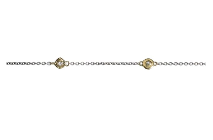 The Points of Light Chain Silver 24in by Waxing Poetic is a delicate sterling silver chain bracelet featuring brass points, each set with two small, round gold accents that encompass crystal gems. The design is simple and elegant, with the gold elements providing a subtle contrast to the shimmering silver chain.