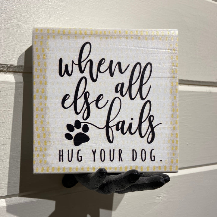 A unique decorative piece by SincereSurroundings, the "Hug Your Dog" sign features the heartfelt message, "When all else fails hug your dog," alongside a charming paw print illustration. Stylishly presented on a black sculpted hand with a white wooden backdrop, it adds an ideal touch to any shelf display in Rock Rapids homes.