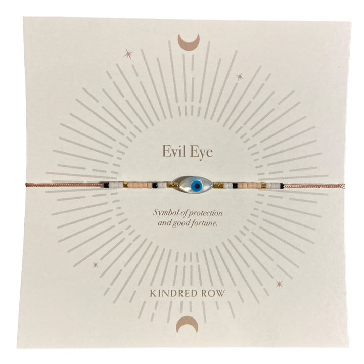 The Evil Eye Cord Bracelet in Dusty Rose, from Kindred Row, features a mother of pearl evil eye bead and is displayed on a card with a sunburst design. The card includes the text "Evil Eye" and "Symbol of protection and good fortune," with "Kindred Row" printed at the bottom.