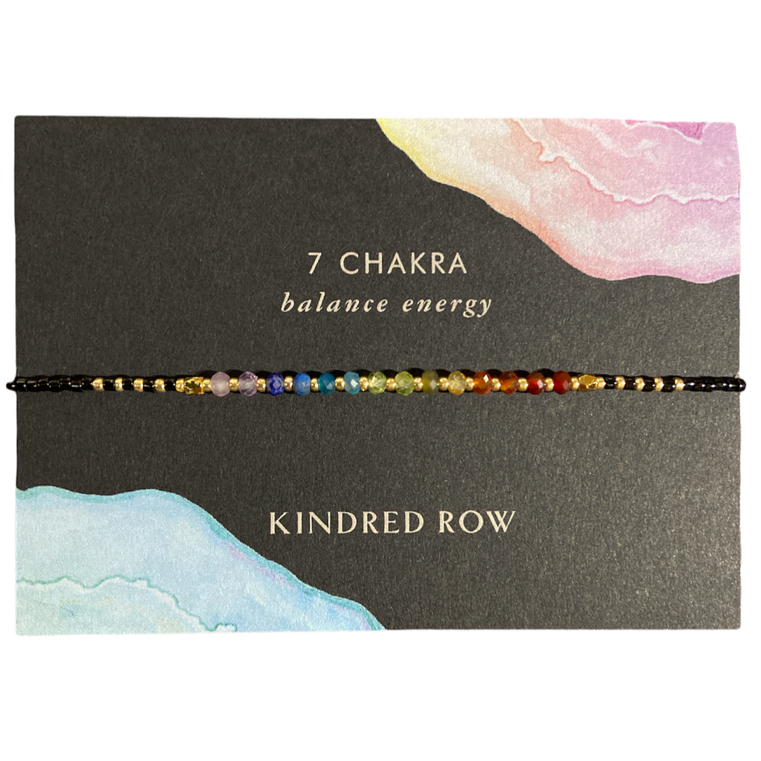 The Chakra Healing Gemstone Stacking Bracelet by Kindred Row is a handcrafted piece adorned with multicolored beads crafted from natural gemstones representing the 7 chakras. It is elegantly presented on a card inscribed with "7 CHAKRA balance energy" and "Kindred Row," featuring delicate watercolor designs, and includes an adjustable cord for an ideal fit.